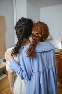Two women with braided hair embrace in a cozy indoor setting, symbolizing friendship and connection.